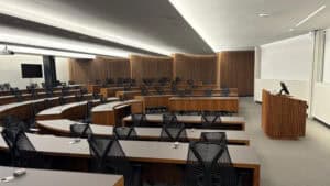 An empty modern conference theatre with tiered seating, wooden panelling, and a podium at the front.