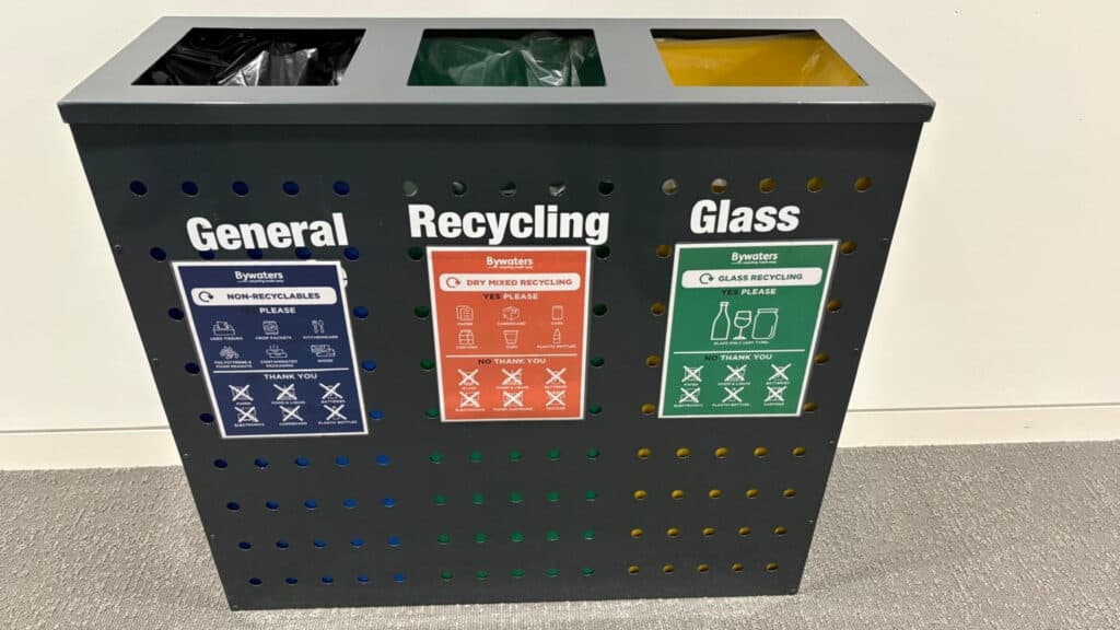 Chicago Booth's dark grey, three-bin waste and recycling station labelled "General", "Recycling", and "Glass" with corresponding signage and coloured slots at the top for waste collection.
