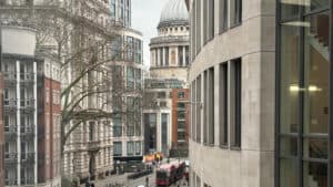 A view of St. Paul's Cathedral dome rising above city buildings, with a red double-decker bus on the street below.