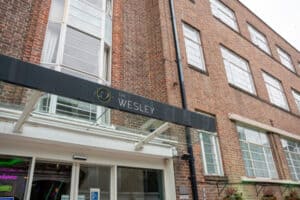 The entrance of The Wesley building with a dark sign above the glass canopy.