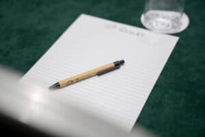 A pen rests on a notepad with The Wesley logo, beside a glass on a green surface.
