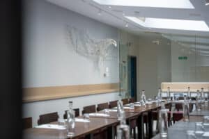 A conference room with a long table set with water bottles and glasses, featuring a wire sculpture of a bird on the wall.
