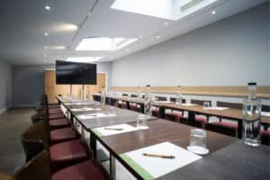 A long conference table with place settings, water bottles, and a large screen at the front of the room.