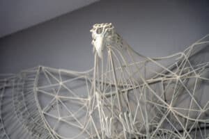 A white wire sculpture of a bird with intricate geometric patterns forming its wings and body.